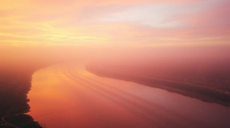 A captivating image of a winding river gently illuminated by a dramatic orange-pink sunset. Soft pastel colors and diffused l