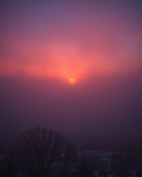 A wide shot captures the serene and atmospheric scene of snowflakes falling during a vibrant sunset. The landscape is shroude