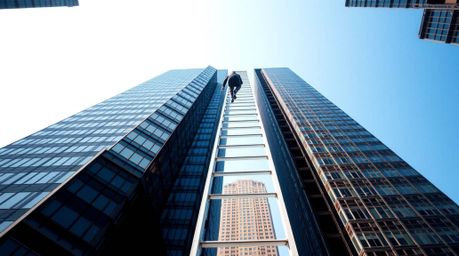 A striking architectural photograph capturing the abstract concept of success. A businessperson ascends a transparent ladder 