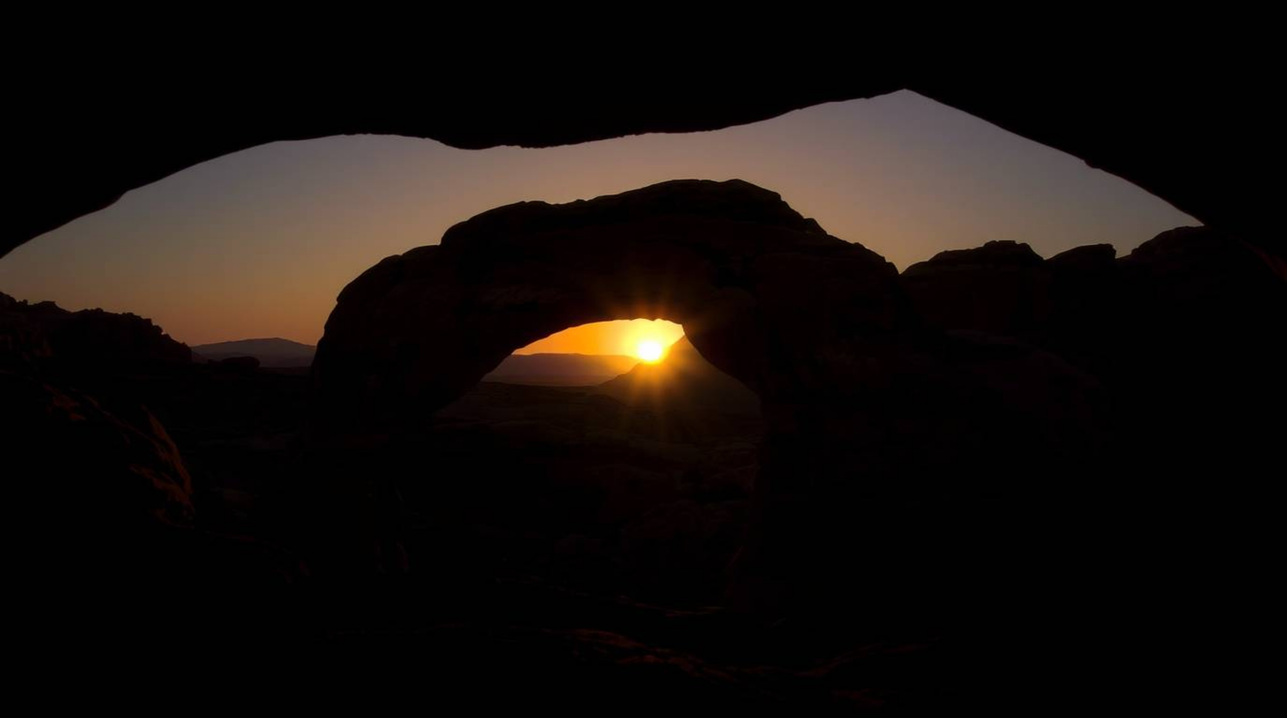 Experience the breathtaking beauty of a desert sunset framed by a natural rock arch, illuminated with dramatic chiaroscuro li