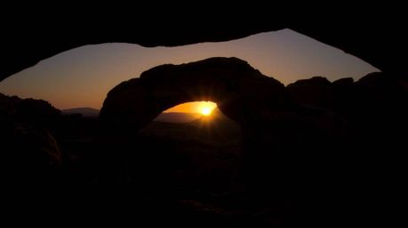 Experience the breathtaking beauty of a desert sunset framed by a natural rock arch, illuminated with dramatic chiaroscuro li