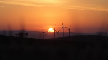 This image captures an extreme macro close-up shot of a breathtaking sunset cascading behind a row of wind turbines perched a