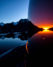 An extreme macro close-up captures a distinct split reflection of a sunset in a glassy fjord. The scene is characterized by s