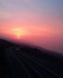 This artwork portrays a cinematic sunset sky over a winding coastal highway, rendered in soft pastel colors. The scene is env