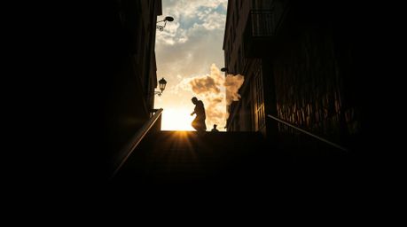 A captivating candid street photography shot features a lone figure ascending a stone staircase bathed in a divine beam of li