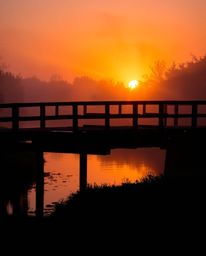 An extreme macro close-up captures the intricate details of an old wooden bridge over a river at sunset. The image is rendere