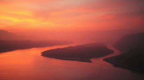 Experience the serenity of a winding river reflecting a breathtaking orange-pink sky, captured in a soft cinematic haze. This