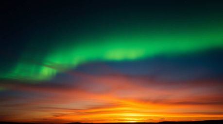 Capture the breathtaking spectacle of the Northern Lights emerging over a vibrant sunset sky. This image showcases intense dr
