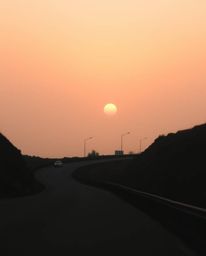 This professional quality, fine art photograph captures a winding coastal highway under a hazy sunset sky, enveloped in a sof