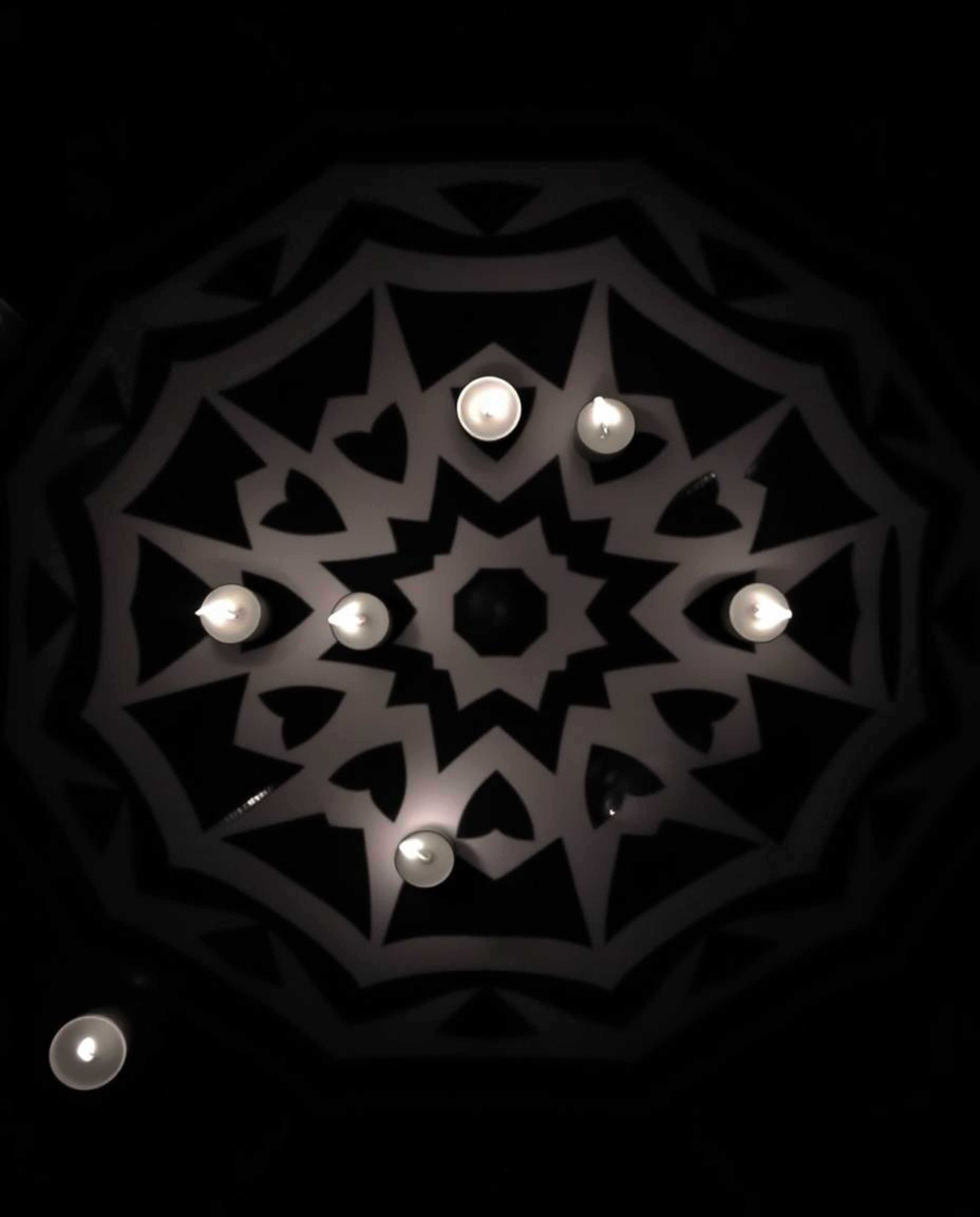 Experience the allure of a top-down black and white image showcasing warm candlelight illuminating a geometric optical illusi