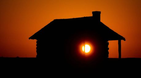 Capture the essence of a silhouetted old wooden cabin at sunset with a strong, moody style. Backlighting creates low contrast