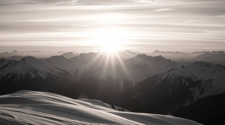 A timeless and elegant black and white photograph captures snow-covered mountains bathed in the soft glow of a pastel sunset.