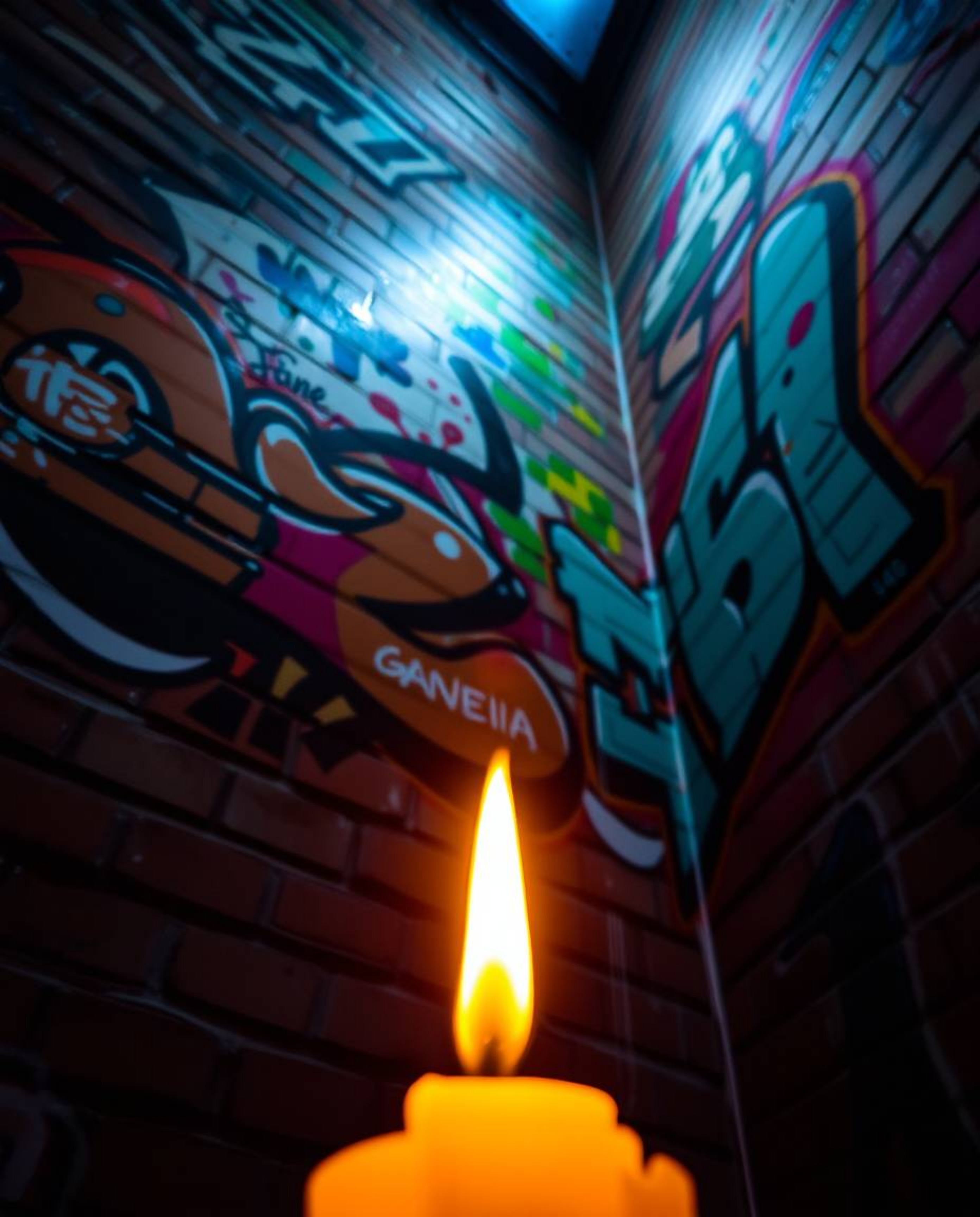 Warm candlelight illuminates colorful graffiti splashes on a brick wall, creating a dramatic upward view of the street art ae