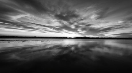 A captivating close-up photograph showcases a serene lake mirroring the vibrant hues of a sunset sky.  The image emphasizes t