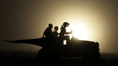 A striking image of a prehistoric family silhouetted against a powerful light source while riding in their dinosaur car. The 