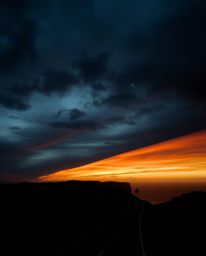 This is a high-resolution stock photo depicting a sunset sky over a winding coastal highway, distinguished by its unique and 
