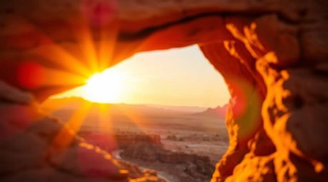 Experience a breathtaking desert sunset framed by a natural rock arch. The sharp details of the arch contrast beautifully wit