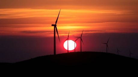 Capture the magic of a dramatic sunset behind a row of wind turbines perched atop a rolling hill. This low-angle perspective 
