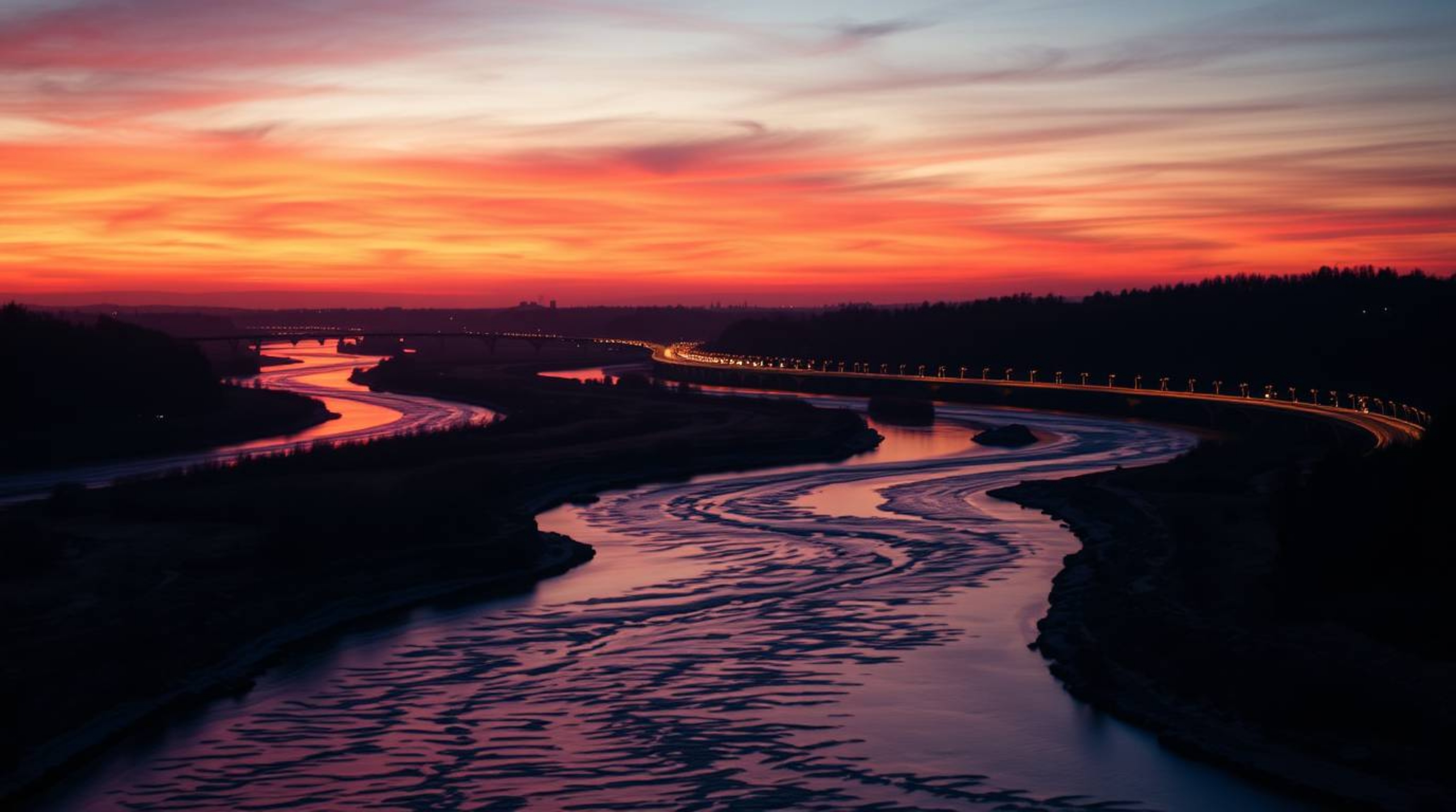 A captivating close-up shot features a winding river bathed in the vibrant glow of an orange-pink sky, set against a backdrop