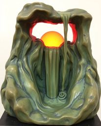 A cast bronze sculpture depicting a sun setting behind a dramatic waterfall, finished in soft pastel colors with an antique p