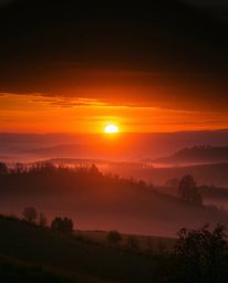 This image captures a Tuscany sunset over misty rolling hills, distinguished by its warm autumnal colors and intense, dramati