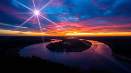 A captivating image of a winding river glowing under a dramatic orange-pink sky.  The bright lens flare effect enhances the v