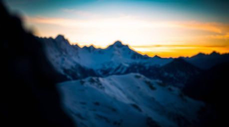 A stunning chiaroscuro photograph captures snow-capped mountains bathed in the soft glow of a pastel sunset.  The image featu