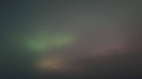 A stunning long exposure photograph captures the ephemeral beauty of the Northern Lights emerging over a vibrant sunset sky, 
