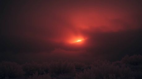 A captivating surreal infrared photograph depicting fog-covered hills bathed in the ethereal glow of a piercing sunset.  The 