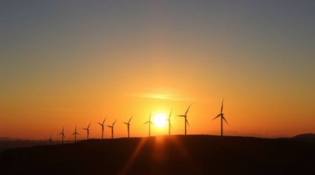 A captivating image showcases a warm, golden sunset radiating behind a picturesque row of wind turbines perched atop a hill. 