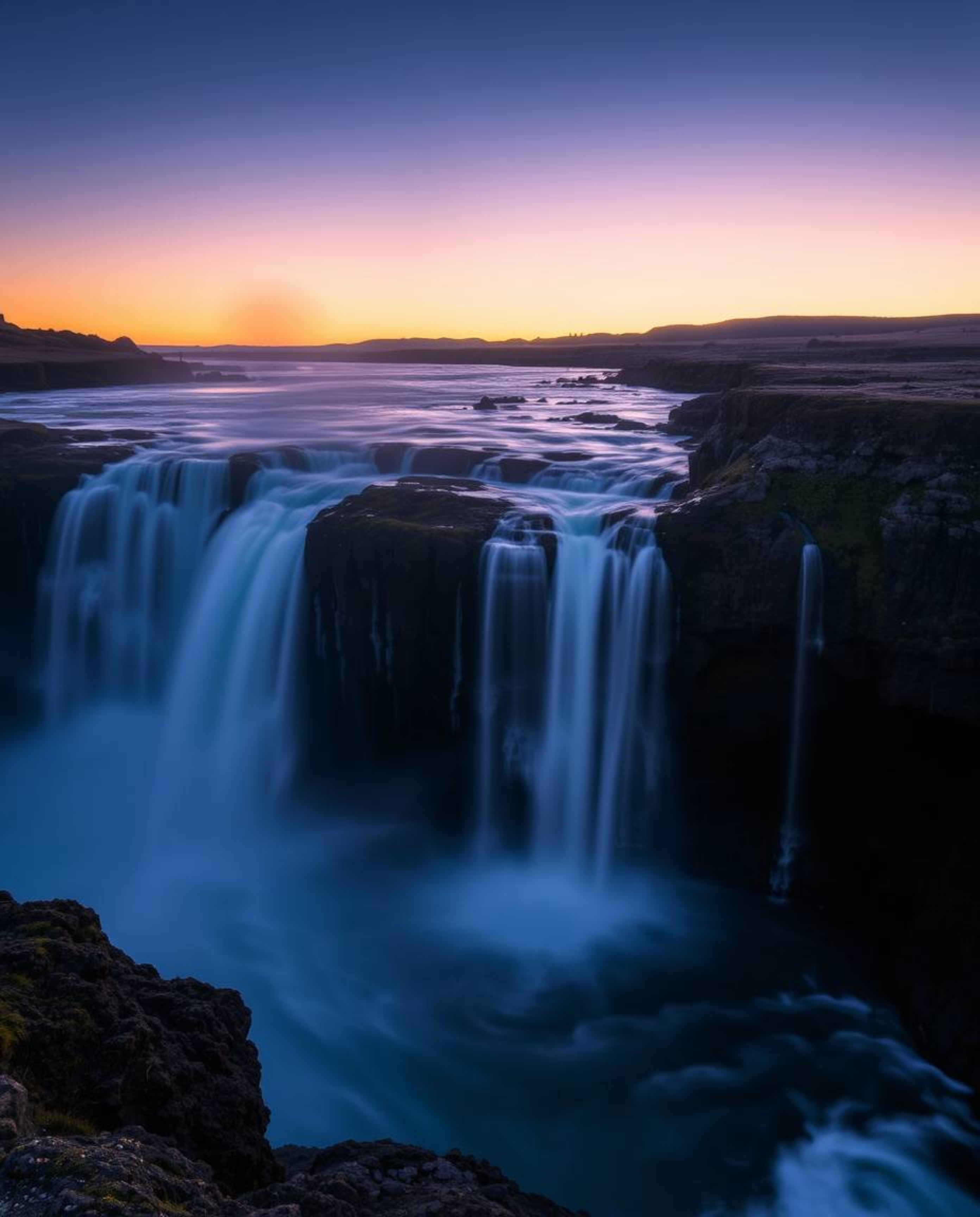 Long exposure photography of a dramatic waterfall at sunset, captured with a cool color palette of blues, greens, and purples