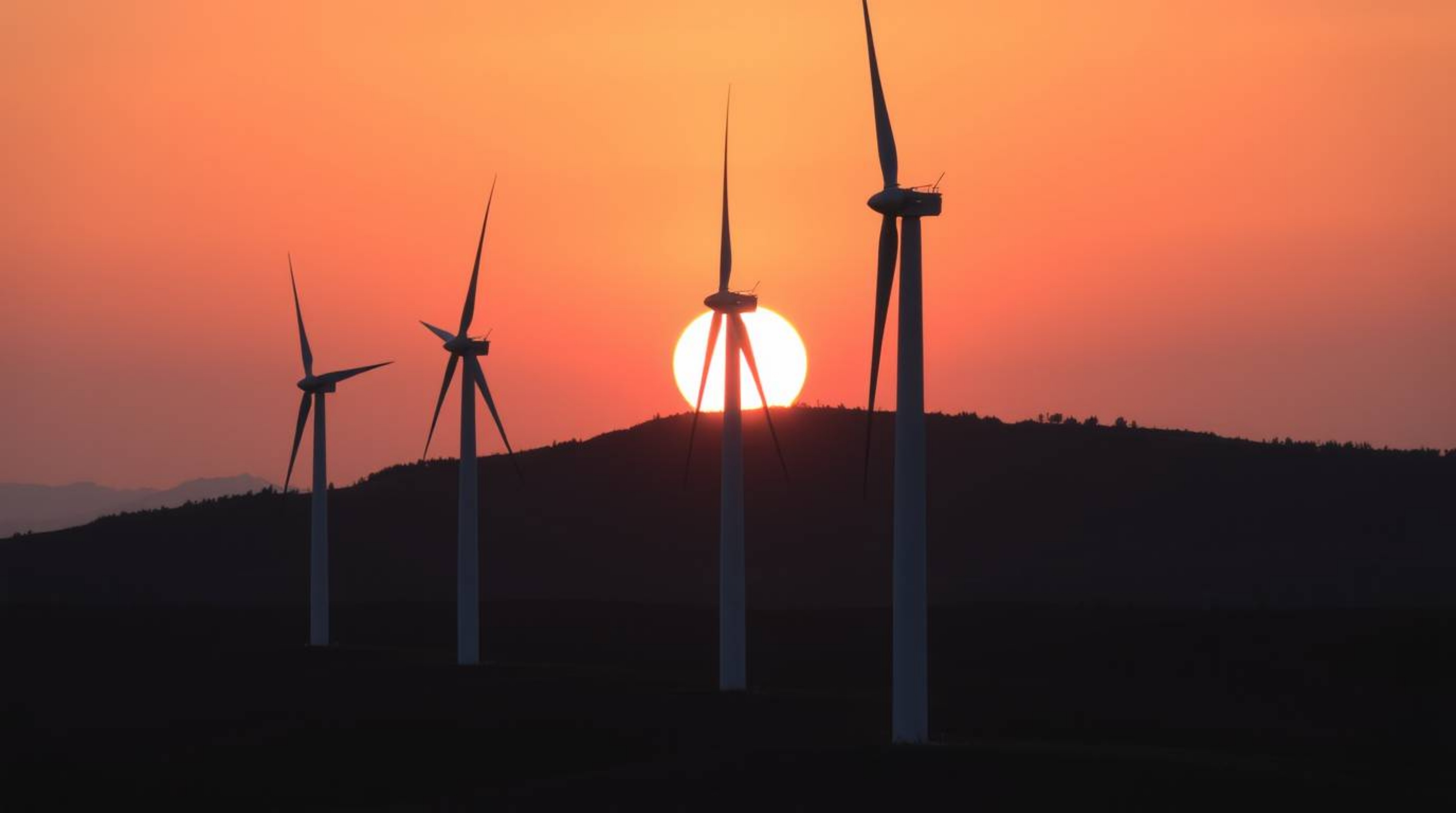 A stunning architectural photograph captures a vibrant sunset cascading behind a row of wind turbines atop a rolling hill.  T