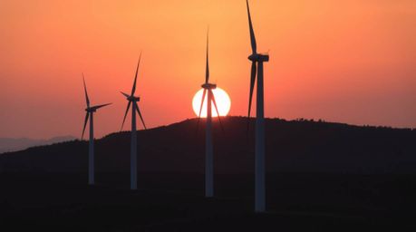 A stunning architectural photograph captures a vibrant sunset cascading behind a row of wind turbines atop a rolling hill.  T
