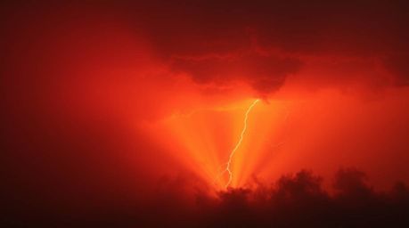 A captivating image showcasing a volumetric lighting effect during a thunderstorm at sunset.  Reds, oranges, and yellows domi