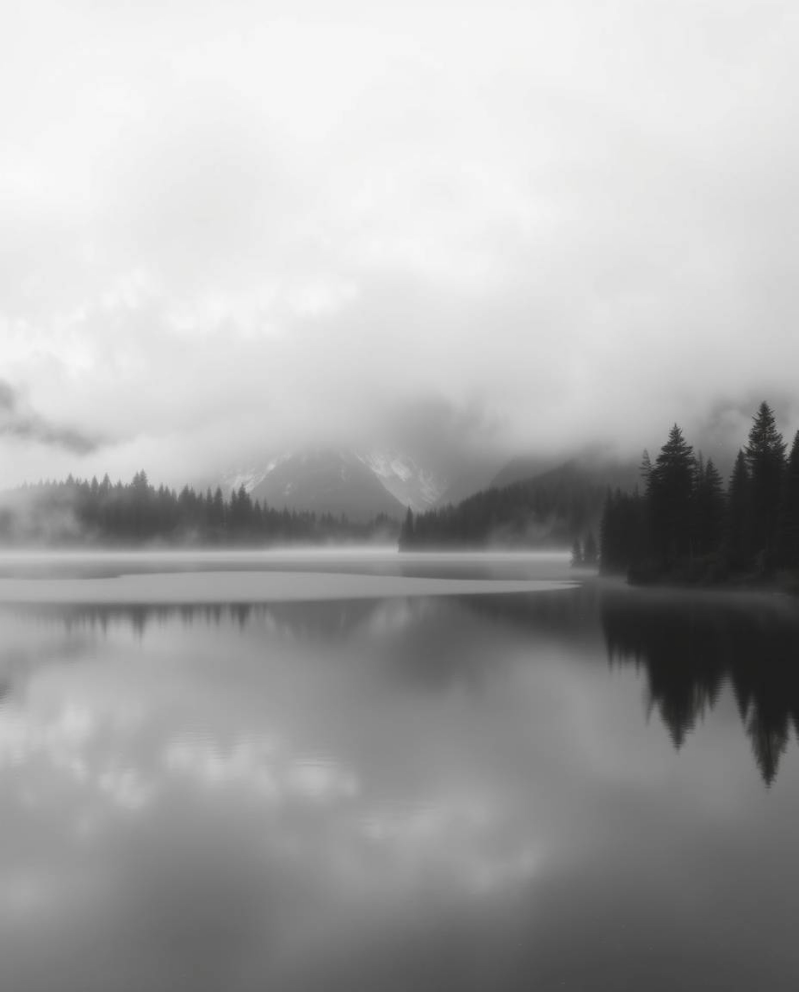 A classic black and white photograph depicts the reflections of fiery clouds in a foggy mountain lake. Characterized by a tim