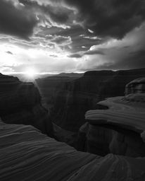 A classic black and white image captures a sunset illuminating sandstone cliffs in a canyon amidst intense and dramatic weath