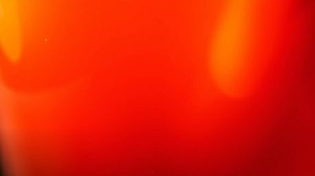 A warm, tight close-up shot of a glass object showcasing its detailed and smooth gradient textures in vibrant reds, oranges, 