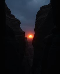 This image portrays a sunset illuminating sandstone cliffs in a canyon through a strong, moody style, creating an eerie and c