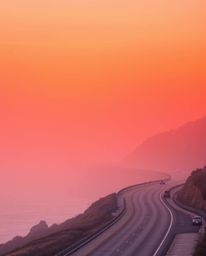 This high-resolution stock photo depicts a hazy, soft-lit sunset sky over a winding coastal highway, imbued with surreal infr