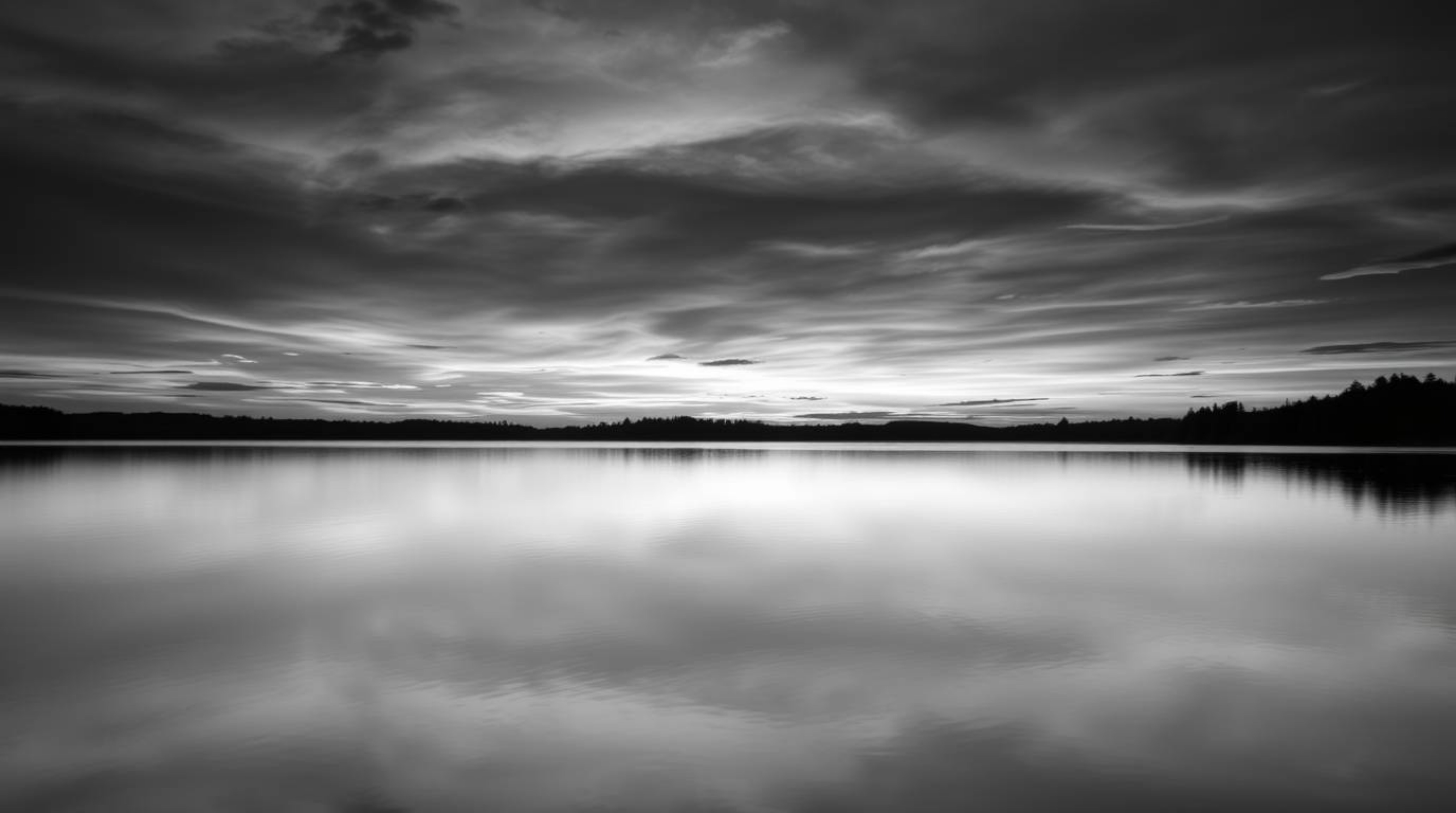 A timeless and elegant black and white photograph depicting a serene lake reflecting the vibrant colors of a sunset sky.  The