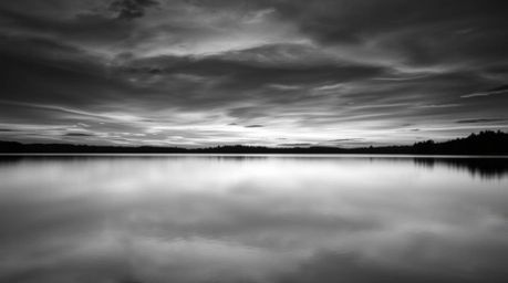 A timeless and elegant black and white photograph depicting a serene lake reflecting the vibrant colors of a sunset sky.  The