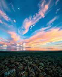 A fine art photograph captures a colorful sky over a coral reef at low tide, rendered in a professional, editorial style. The