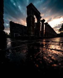 Experience ancient stone ruins at sunset from a dramatic low-angle perspective during a wet, rainy scene. The drizzling rain 