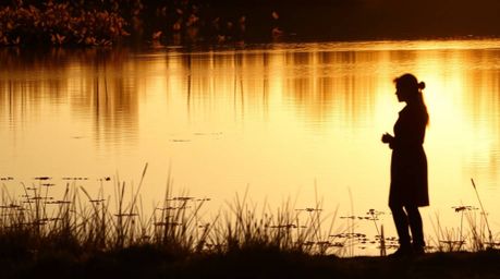 A captivating photograph showcasing a calm pond mirroring a vibrant sunset, infused with warm autumn hues. The silhouetted su