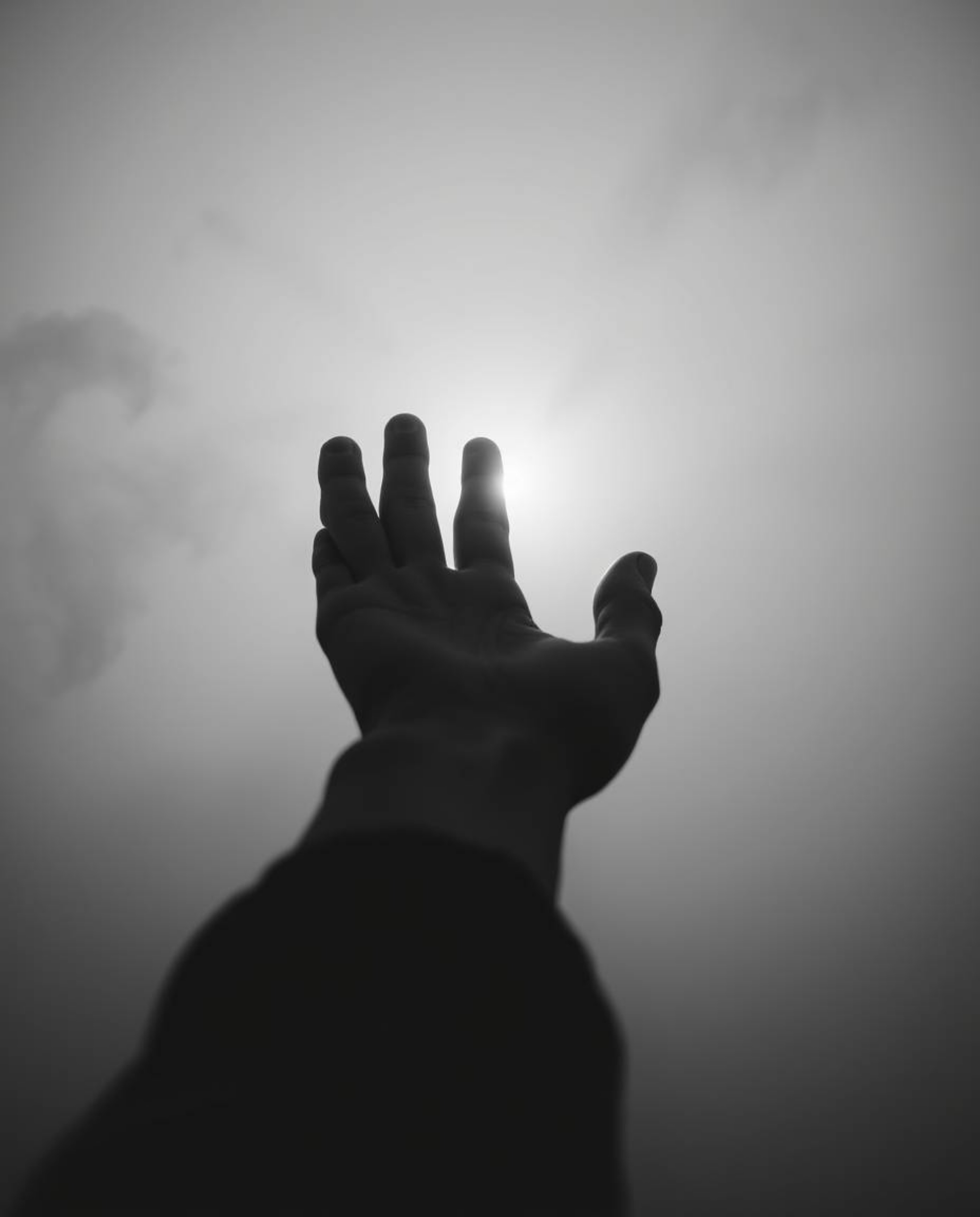A captivating black and white image depicts a hand emerging from darkness, reaching towards a source of light in a thick fog.