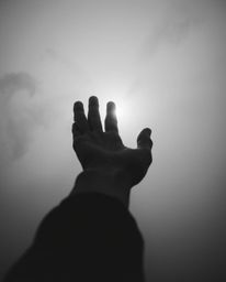 A captivating black and white image depicts a hand emerging from darkness, reaching towards a source of light in a thick fog.