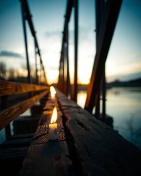An extreme macro close-up captures the intricate details of an old wooden bridge over a river at sunset. The image is rendere