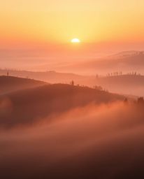 A photograph of a sunset over misty rolling hills in Tuscany, with volumetric lighting creating an ethereal and spiritual vib