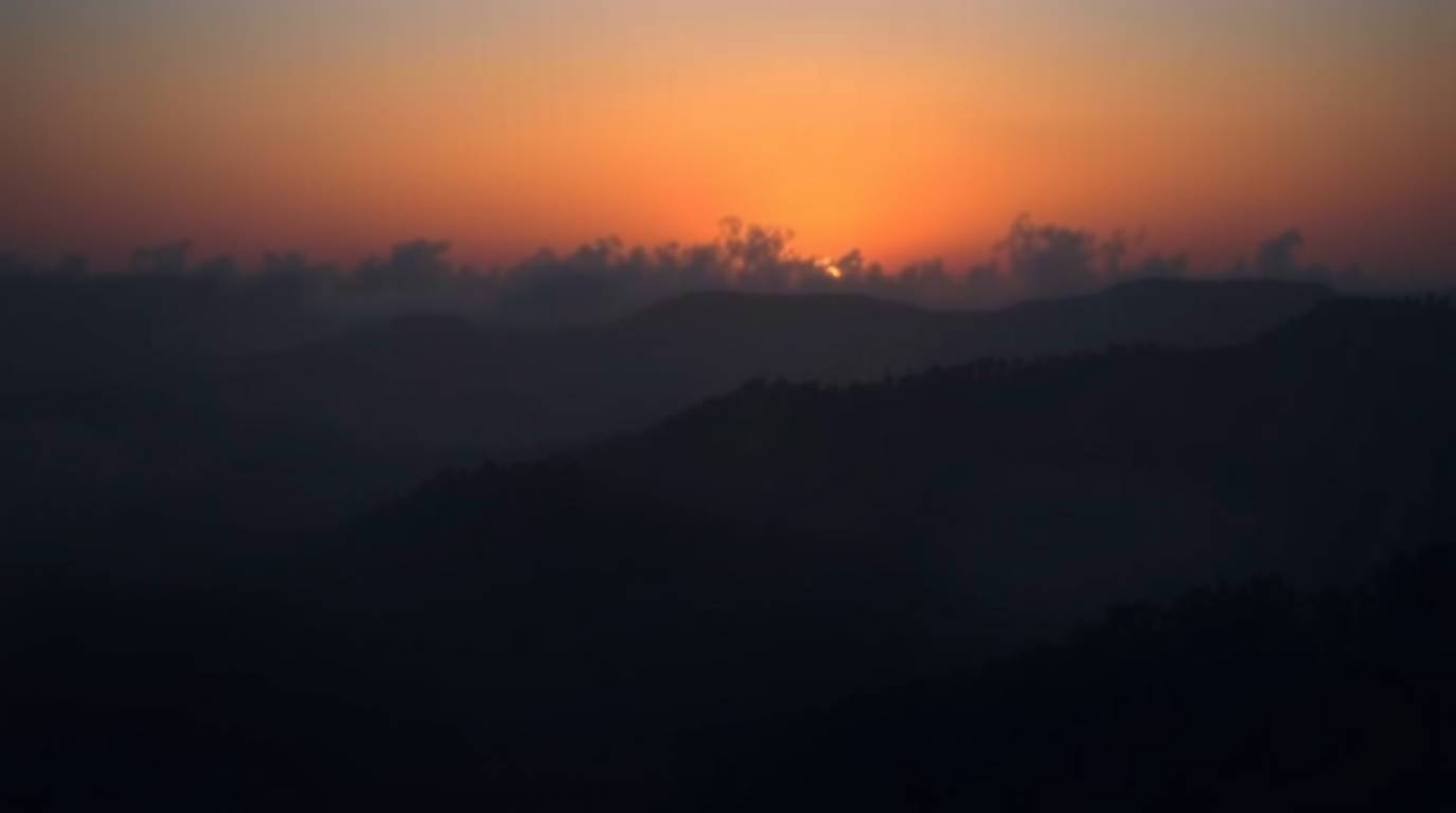 Dramatic fine art photography showcasing intense jet black fog-covered hills with ethereal sunset light breaking through. Dee
