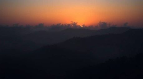 Dramatic fine art photography showcasing intense jet black fog-covered hills with ethereal sunset light breaking through. Dee